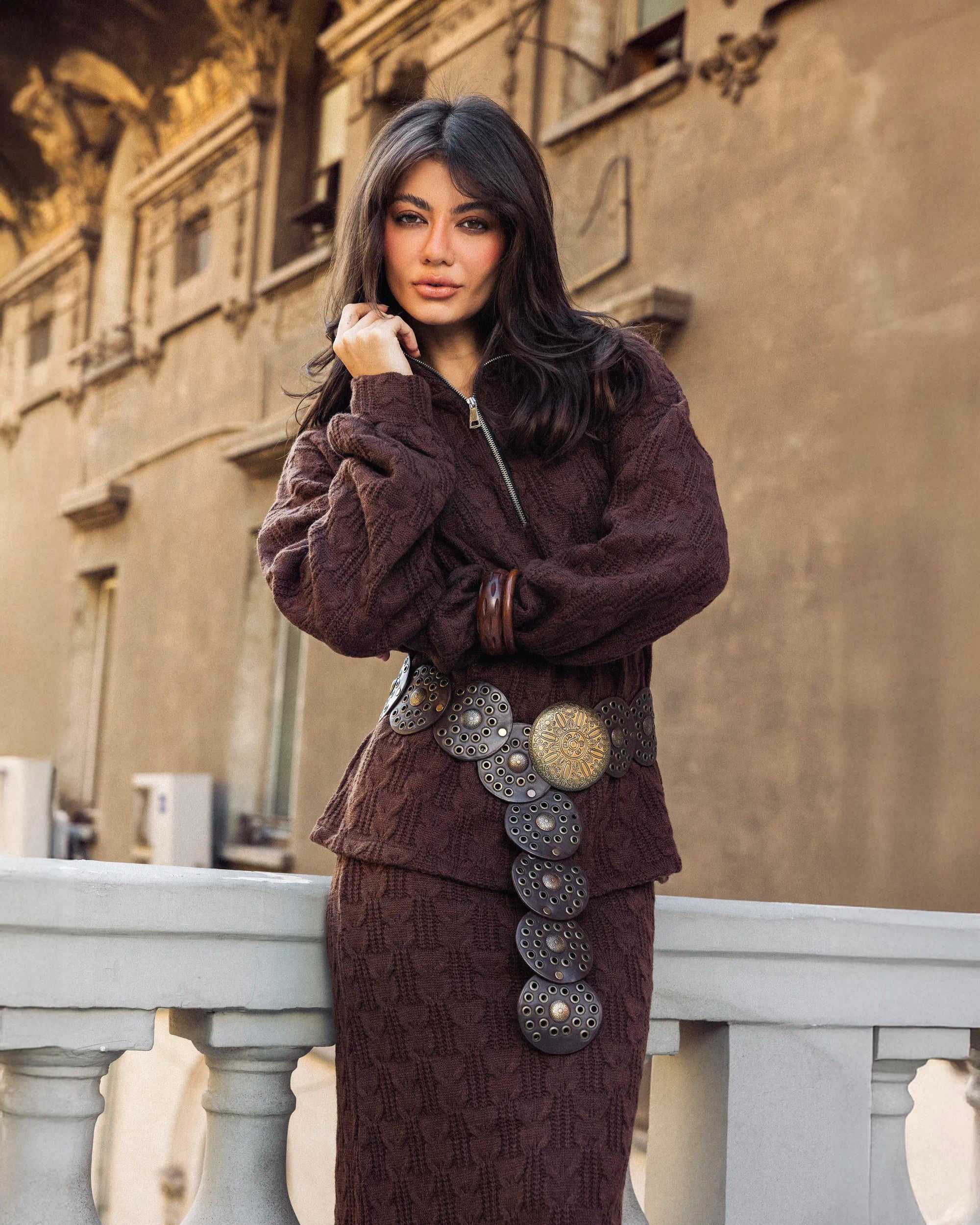 “Model wearing the brown Era Set in a leaning pose highlighting the textured knit fabric and long skirt drape.”