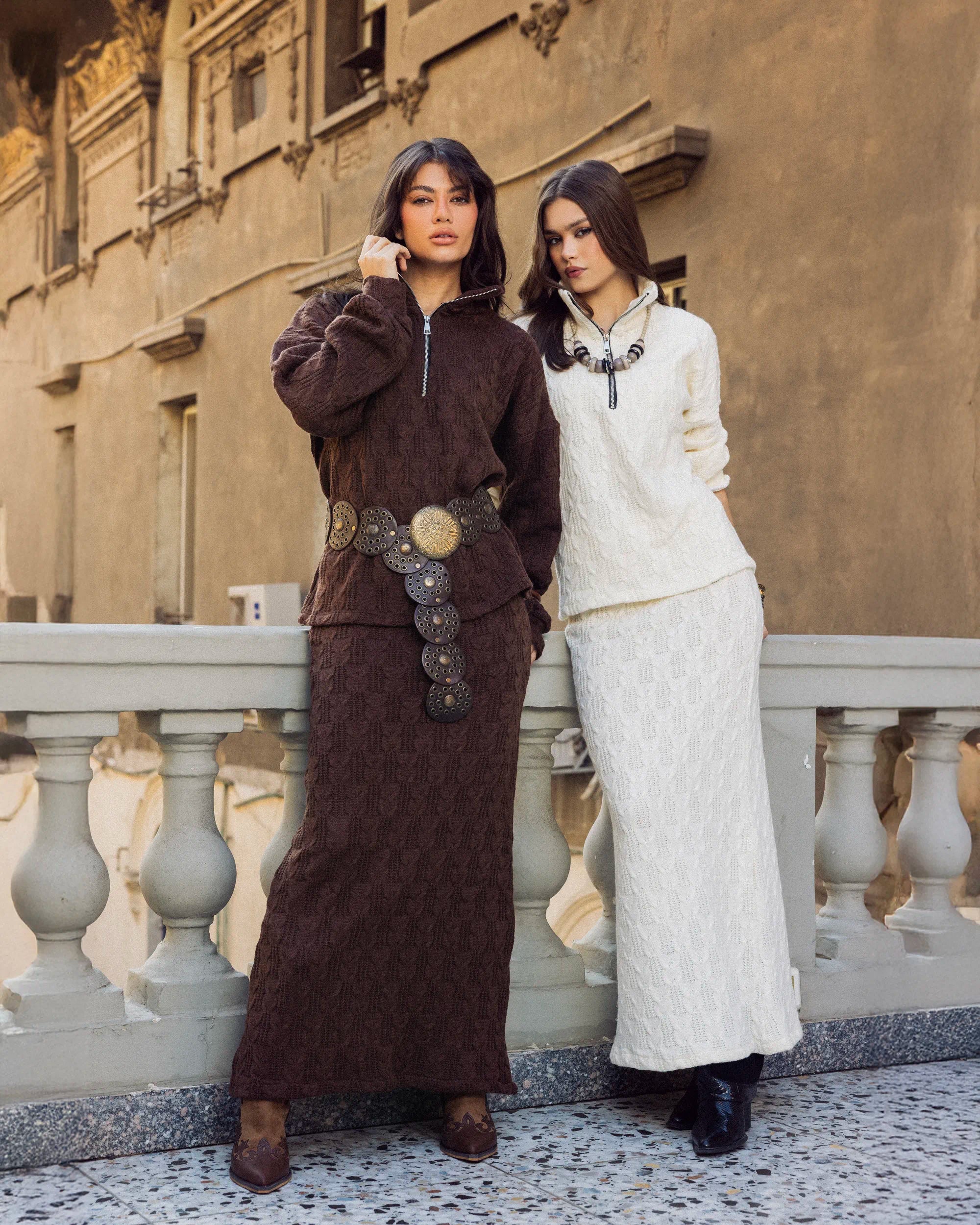 “Two models wearing the Era Set in brown and white, showcasing the textured knit design and modest long skirt.”