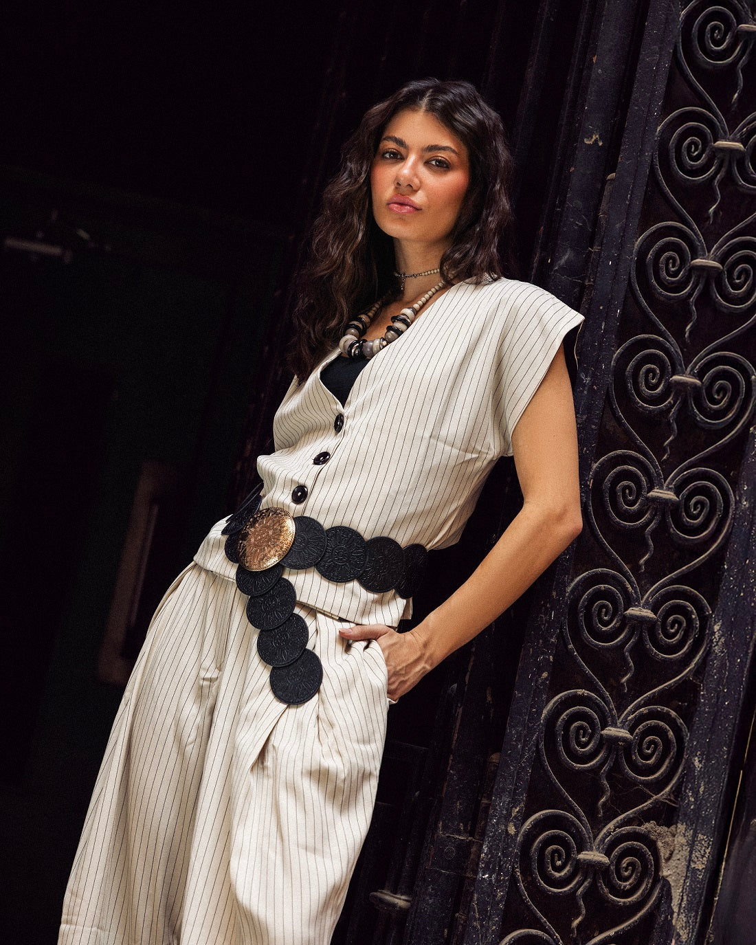 Woman in a white saree with black buttons standing against a dark background