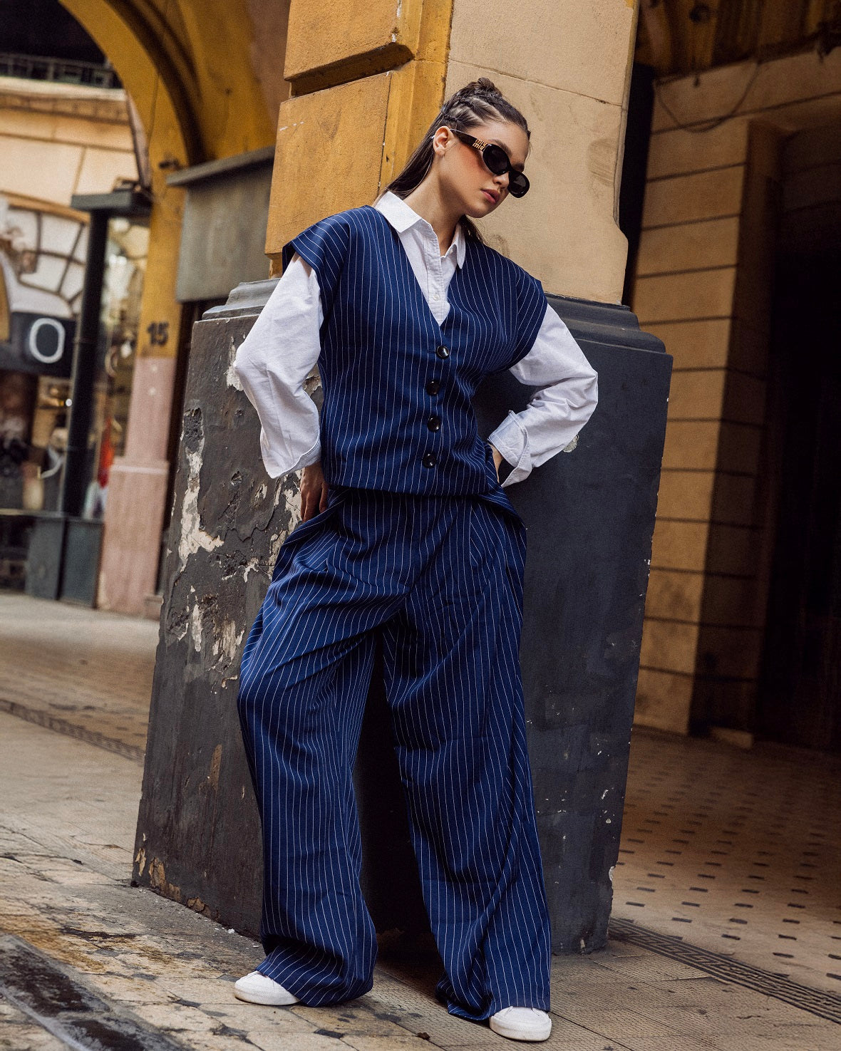 Person wearing a blue pinstripe suit with a white shirt, standing against a textured wall.