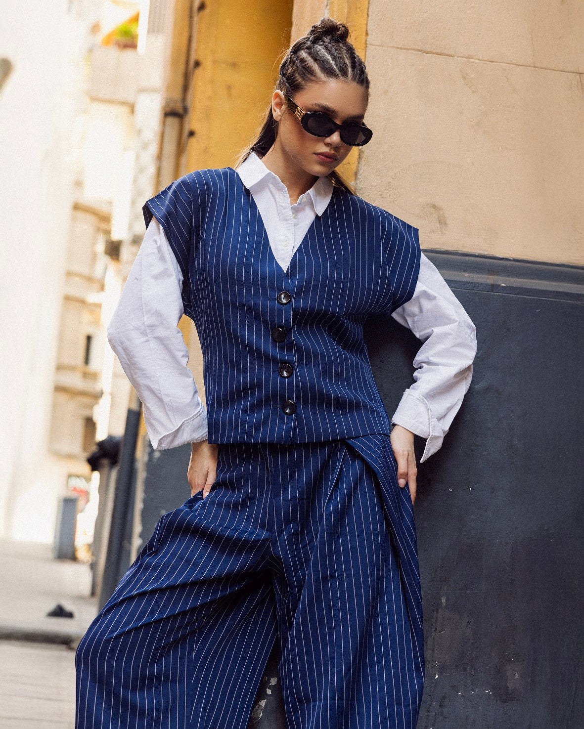Person wearing a blue pinstripe vest and pants with a white shirt, standing against a building.
