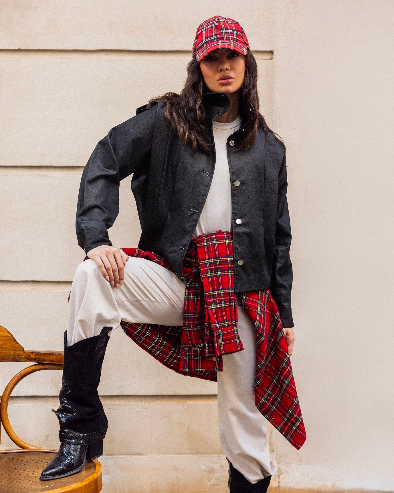 Person wearing a black jacket, white shirt, plaid skirt, and red cap sitting on steps.