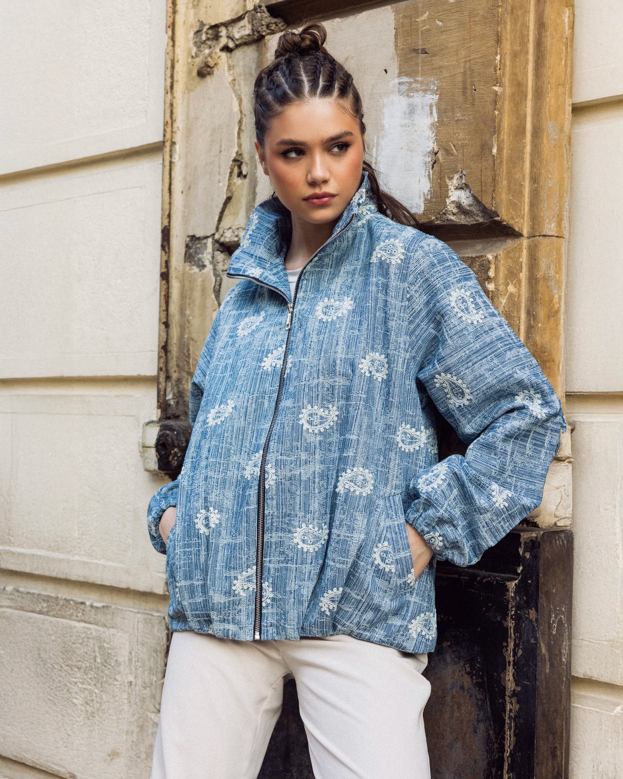 Woman wearing a blue patterned jacket standing against a textured wall.