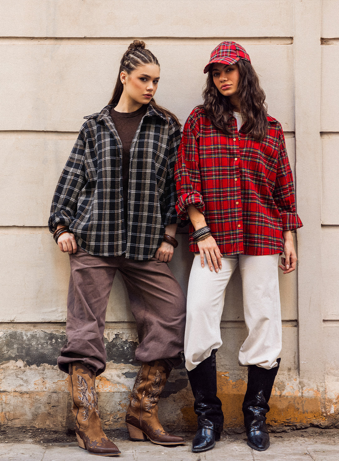 Woman in teal blouse and brown pants leaning against a wall in an urban setting
