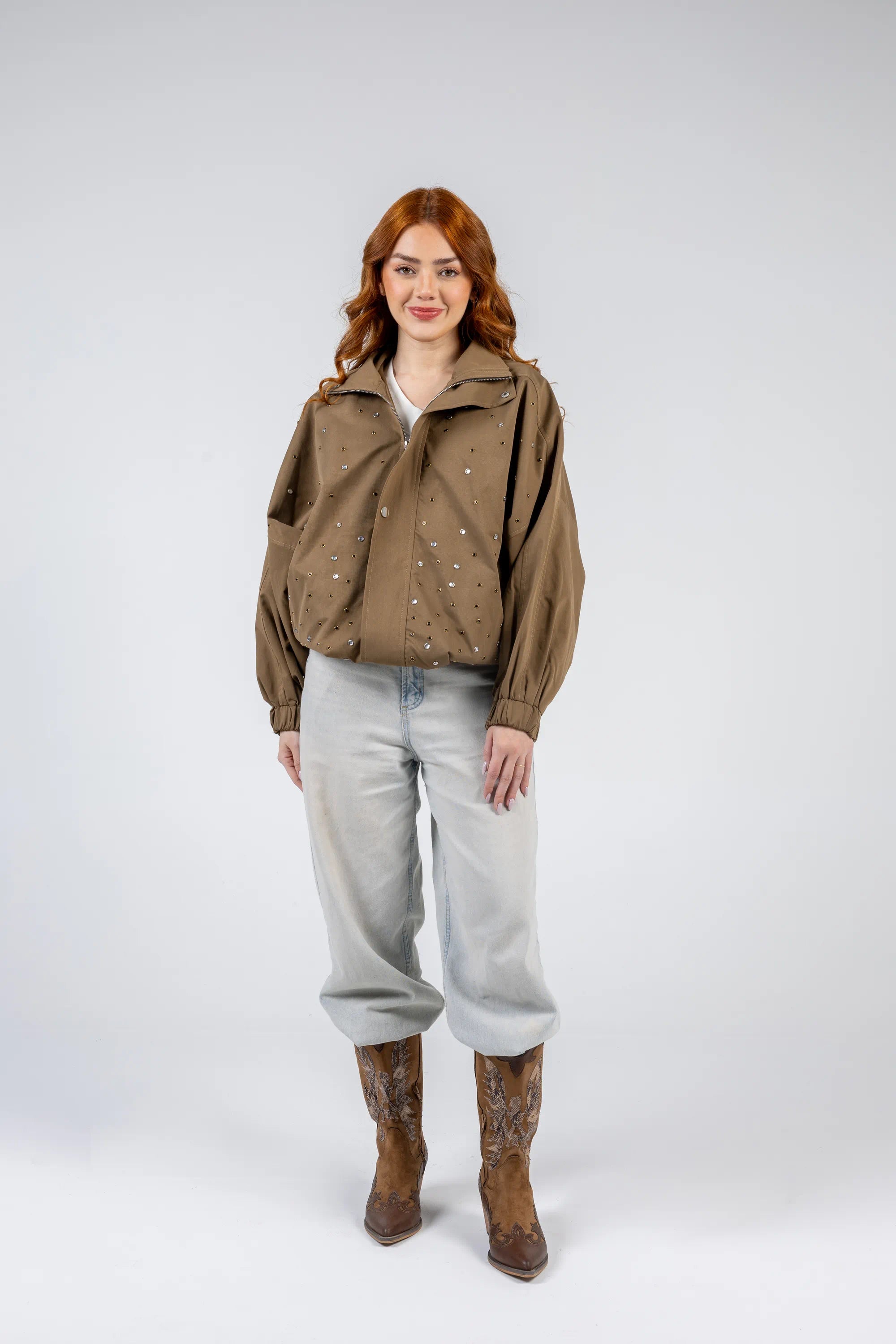 Woman wearing a brown jacket, light blue jeans, and brown boots on a white background