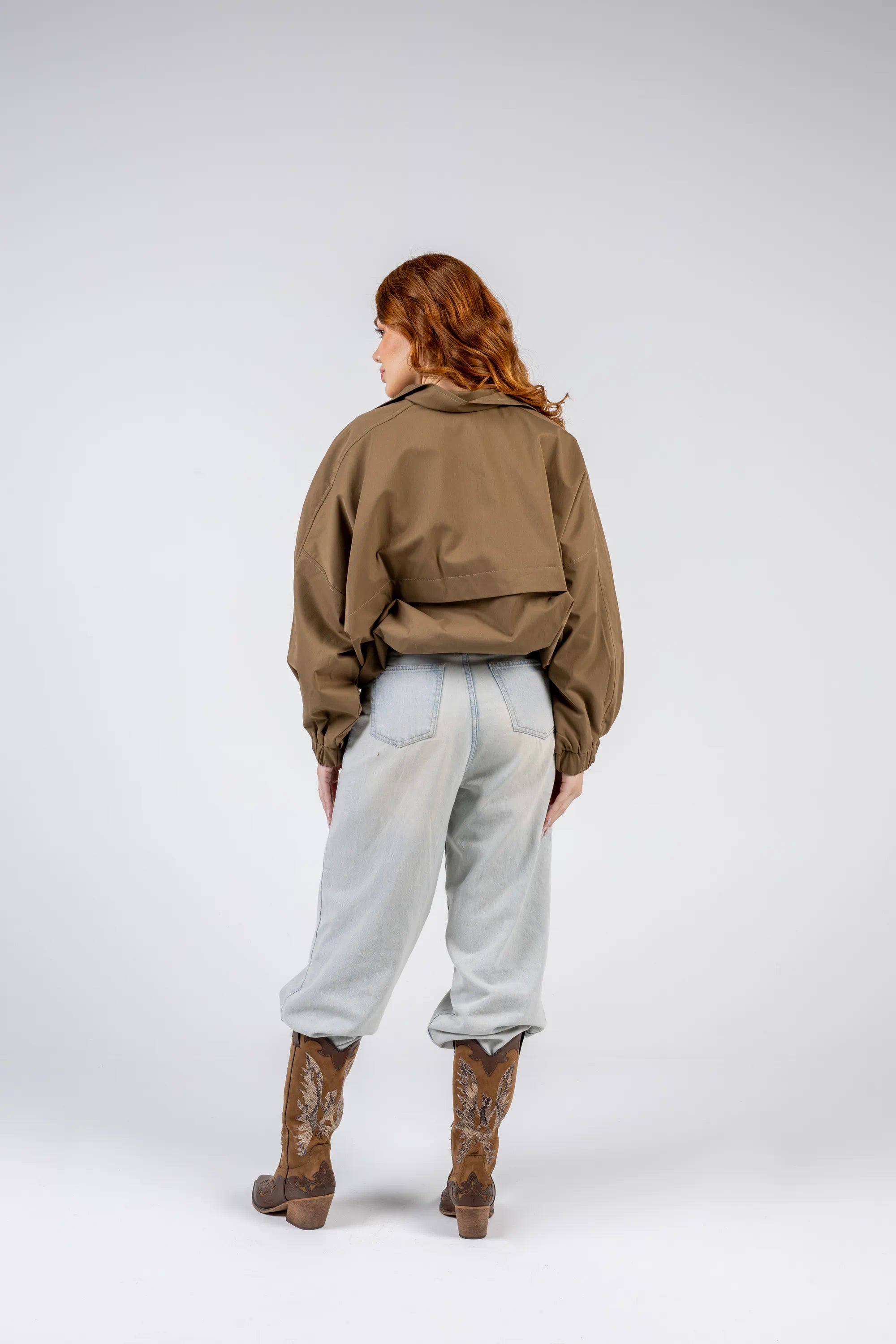 Person wearing a brown jacket, light gray pants, and brown boots on a white background