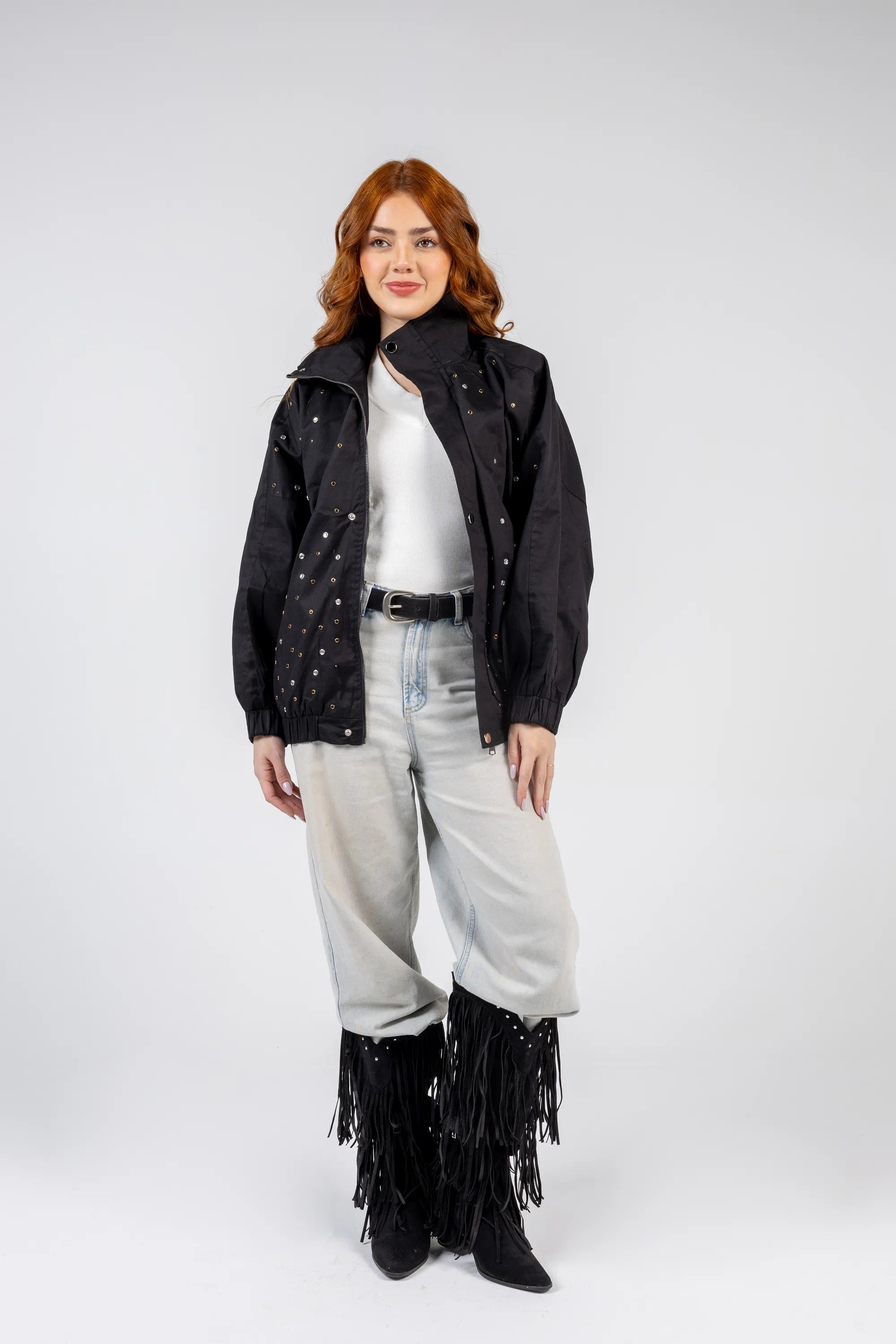 Person wearing a black jacket with star patterns, white shirt, light blue jeans, and black fringed boots on a white background.