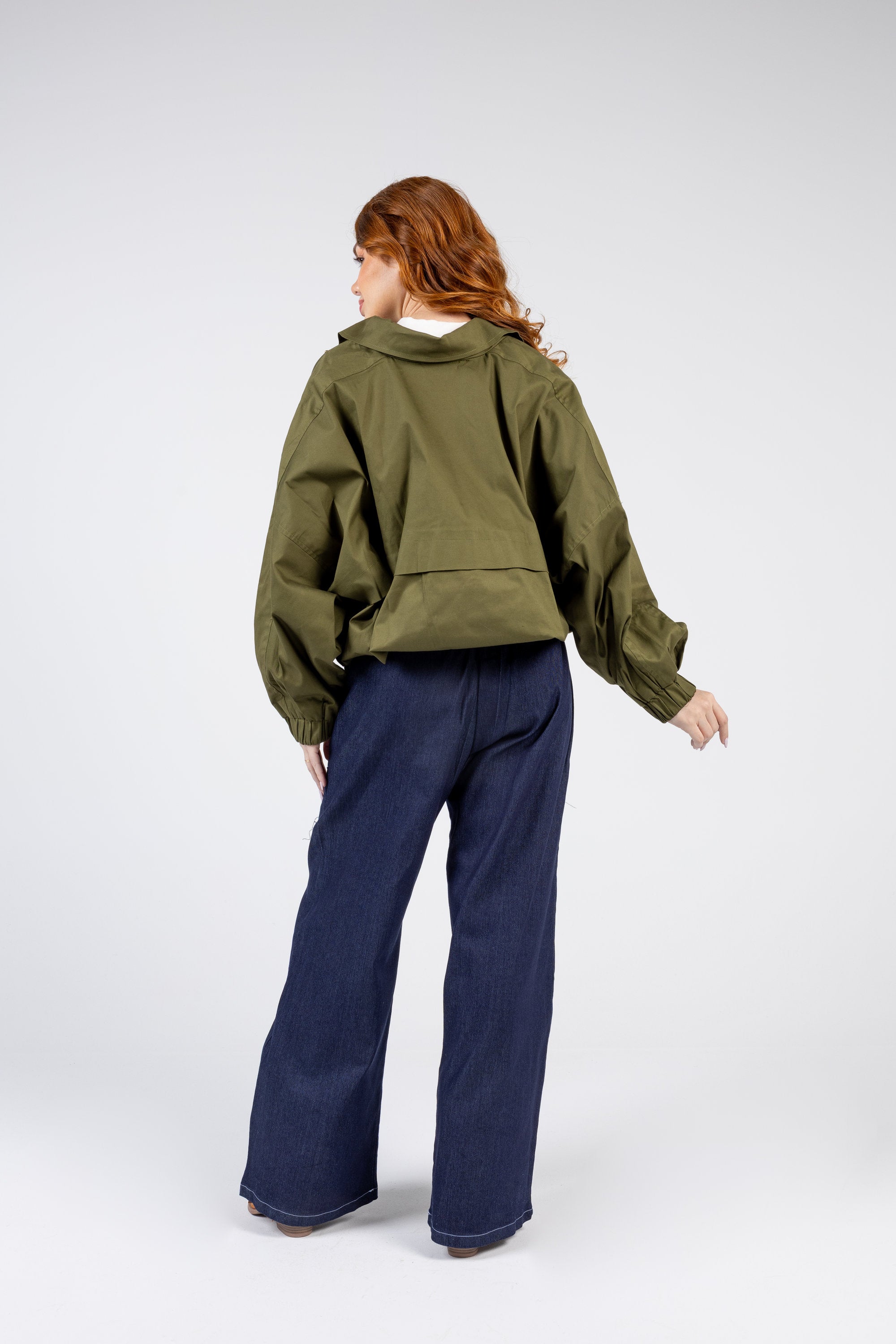 Person wearing an olive green jacket and navy pants on a white background