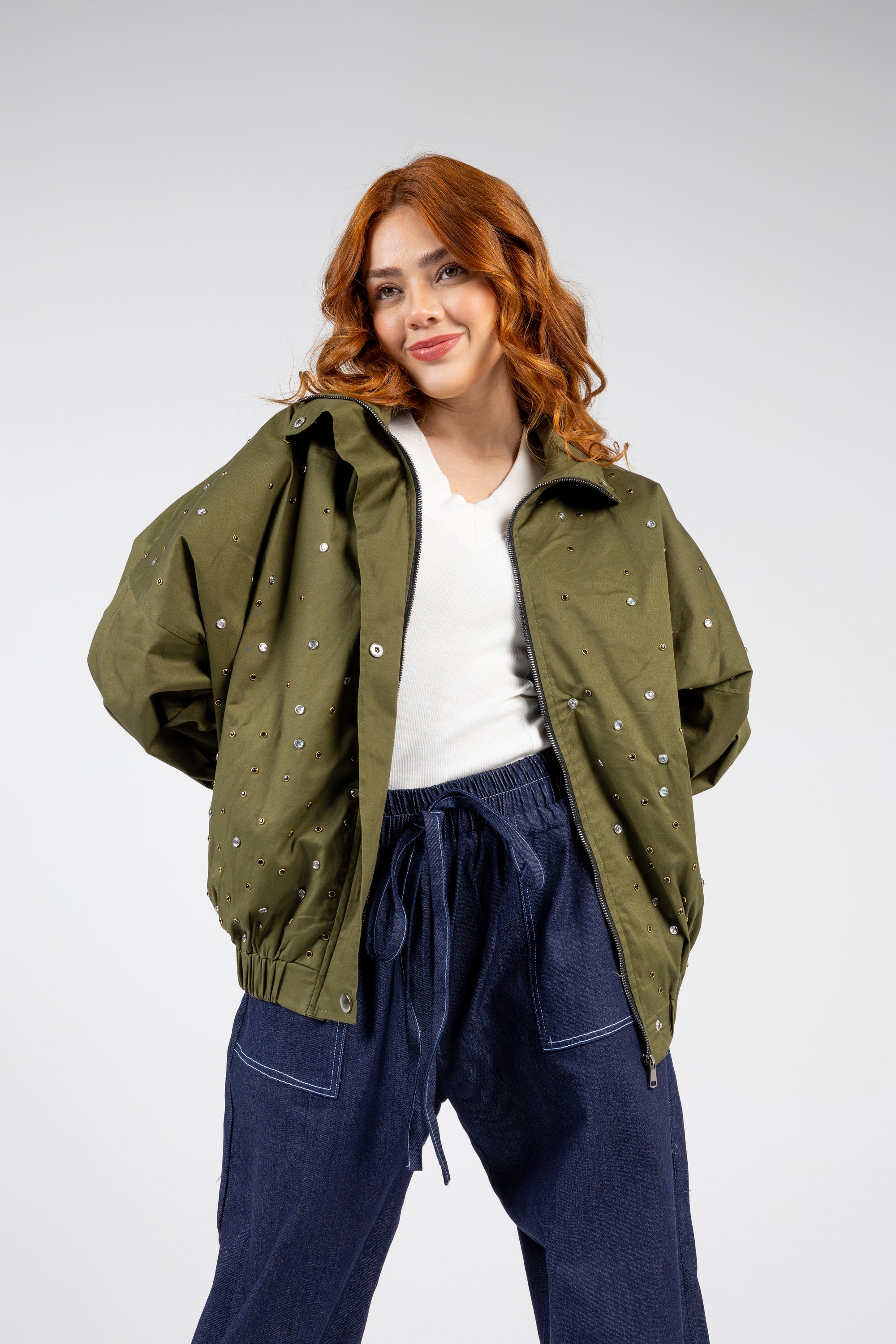 Woman wearing an olive green jacket with white buttons on a plain background