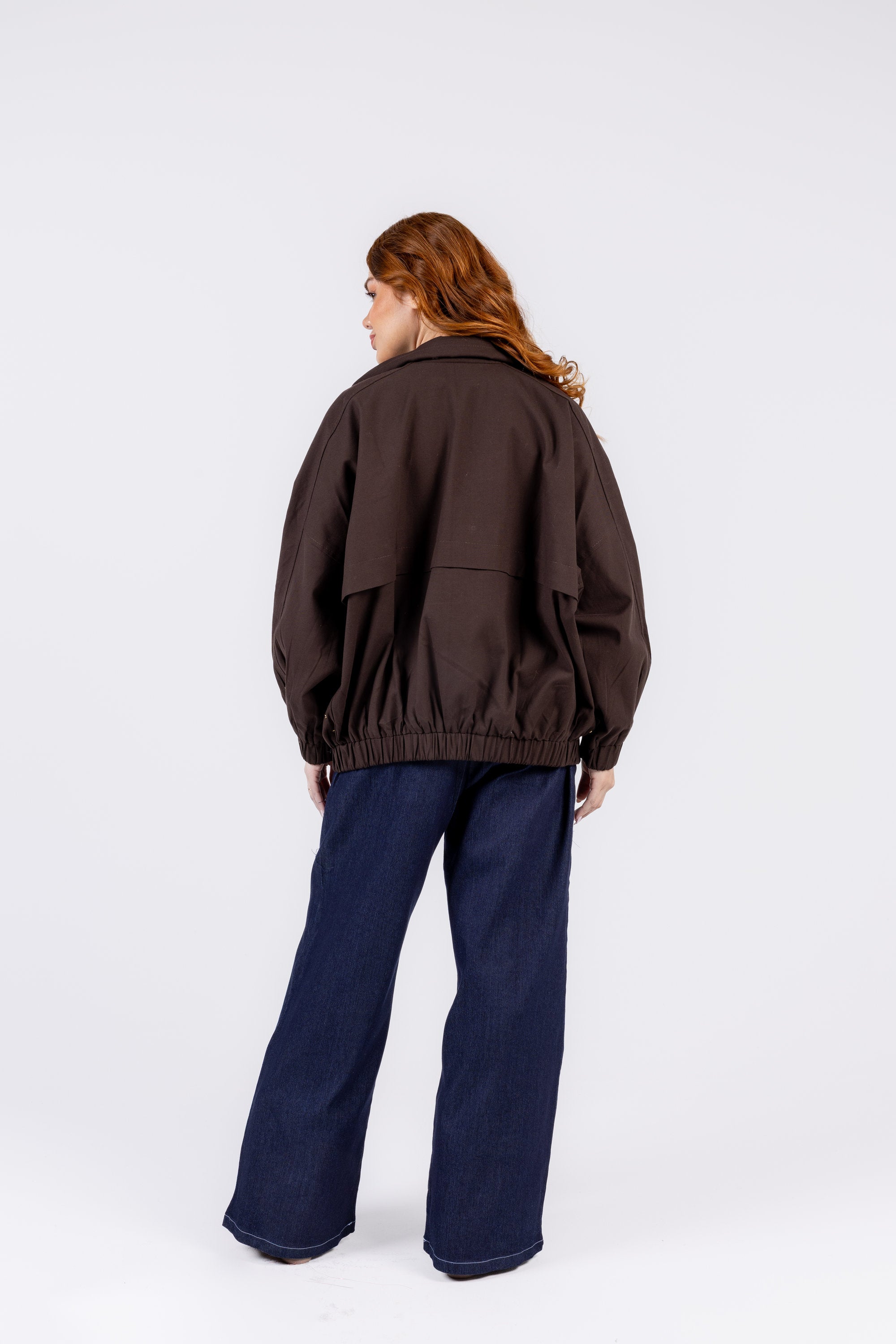 Person wearing a brown jacket and blue pants on a white background