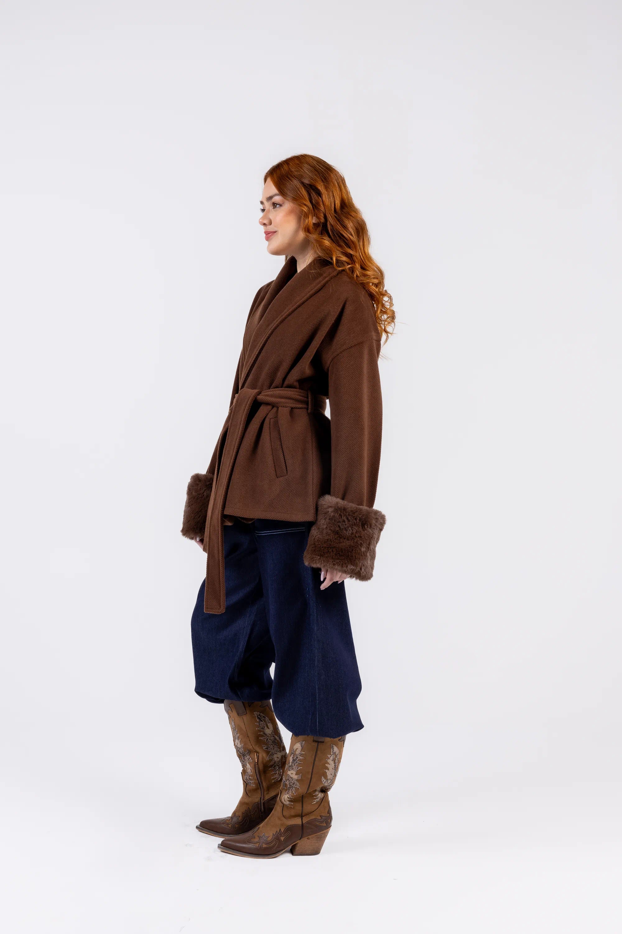 Woman wearing a brown coat with fur trim and blue pants on a white background