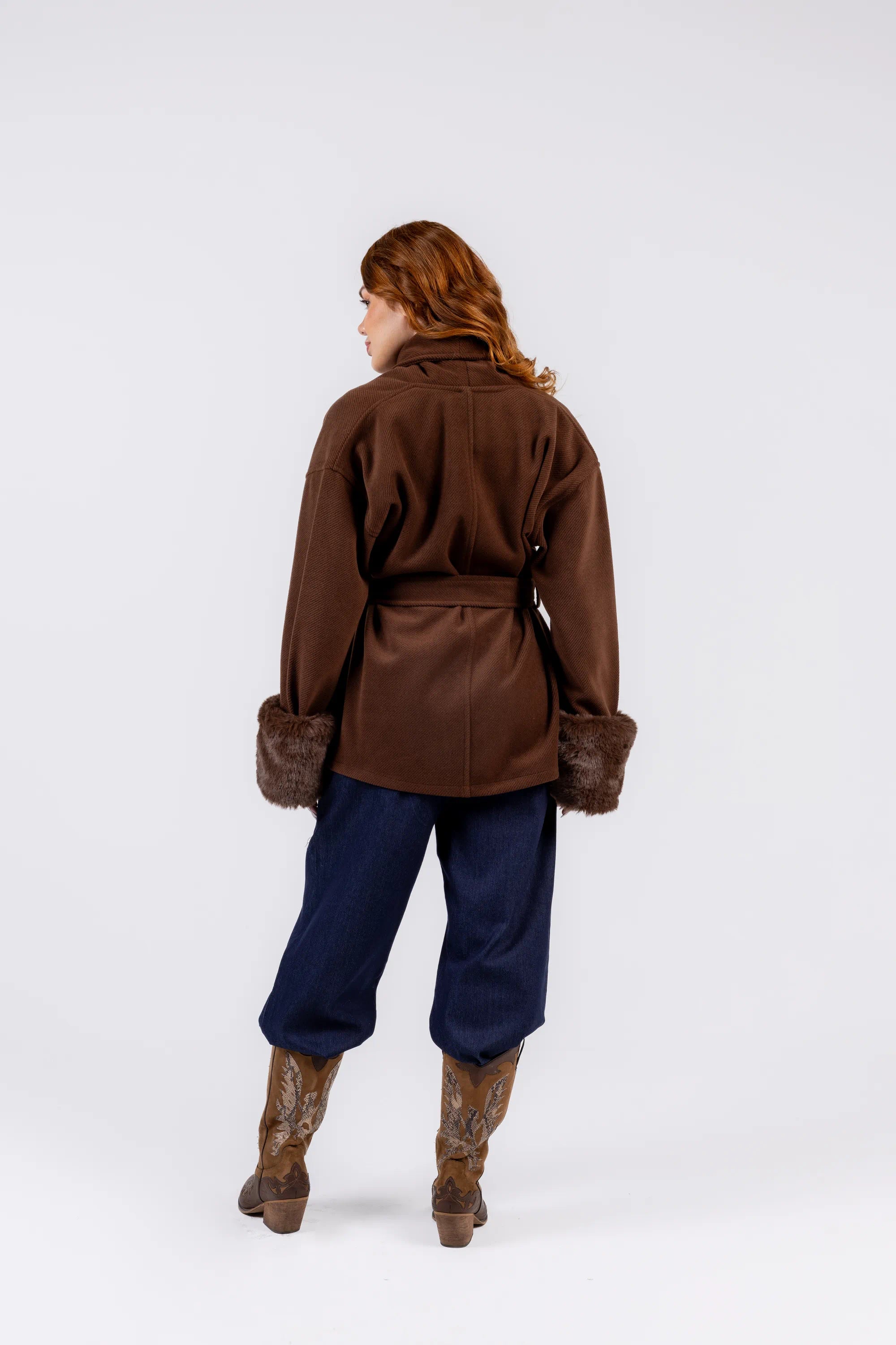 Person wearing a brown coat and blue pants on a white background