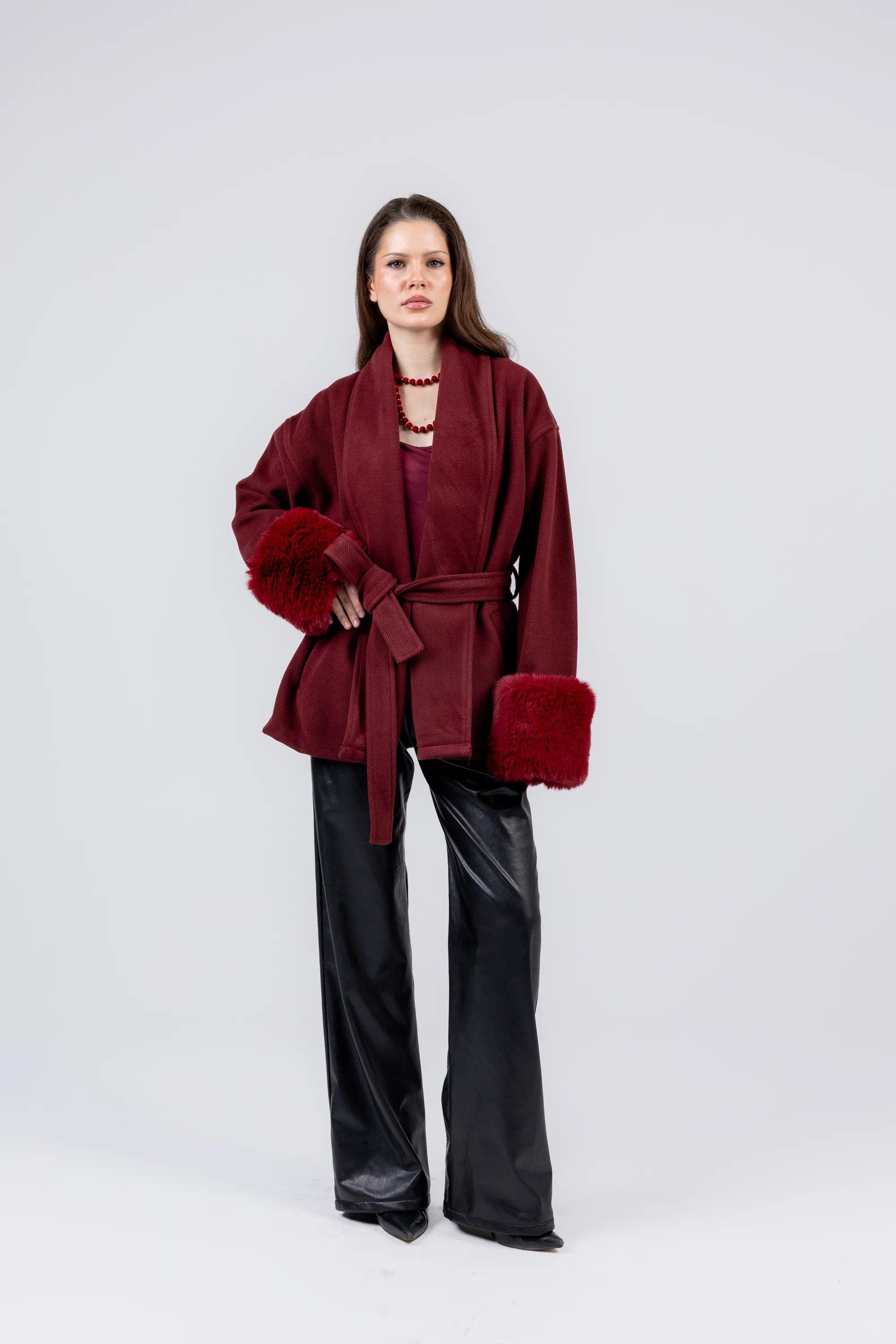 Woman wearing a burgundy coat with fur trim on a white background