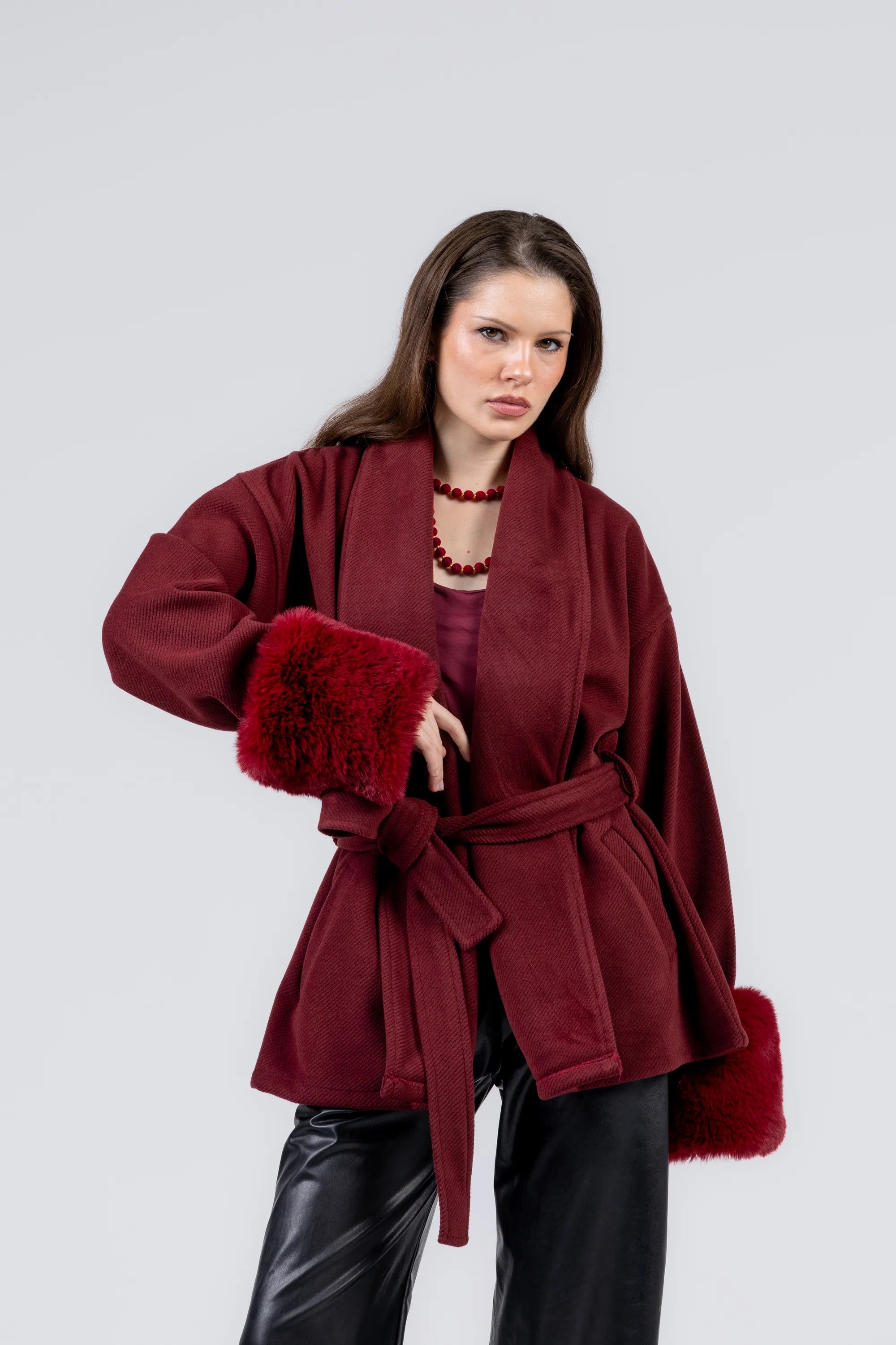 Woman wearing a burgundy coat with fur cuffs on a light gray background