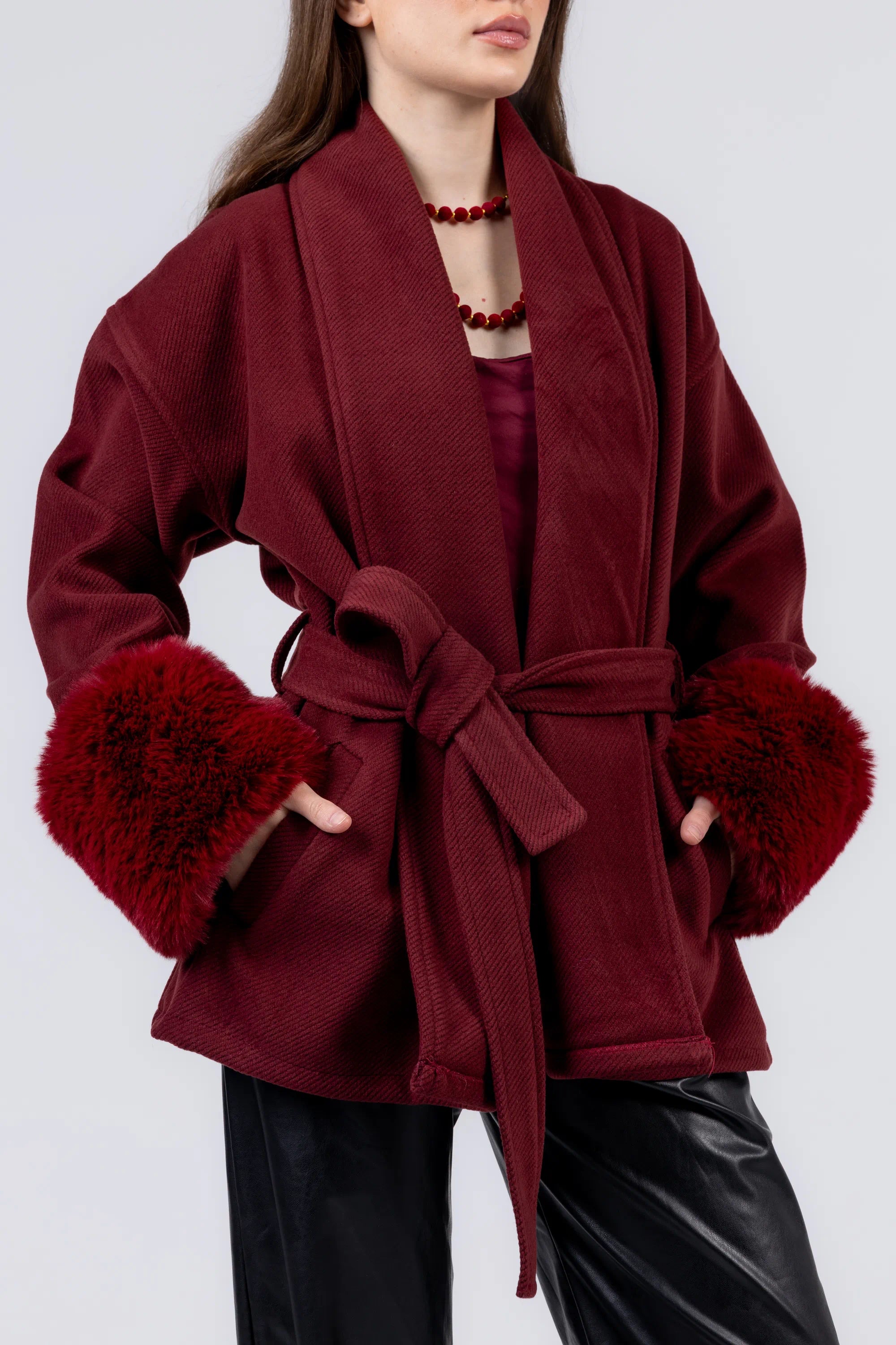 Red coat with fur cuffs worn by a person on a white background