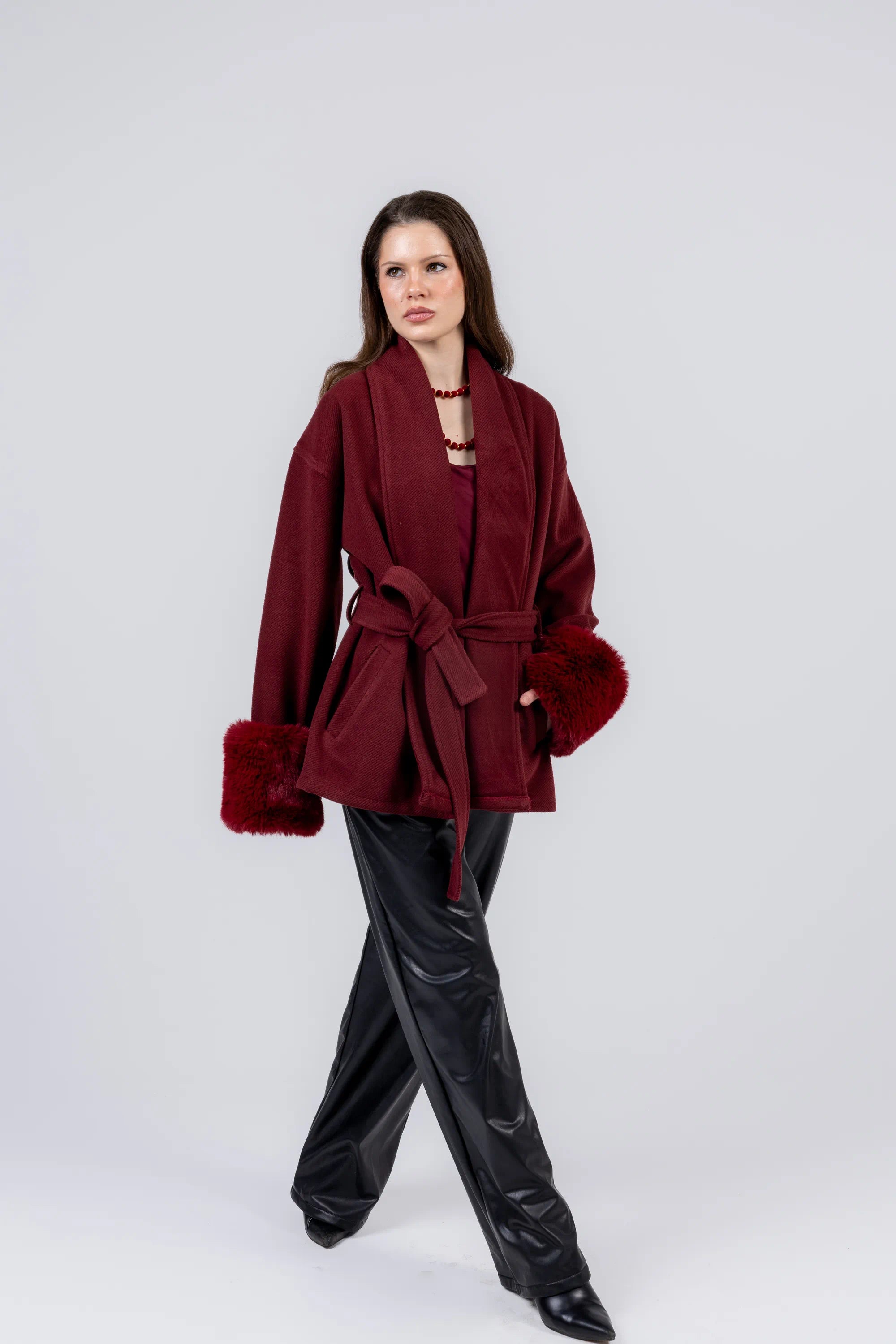 Woman wearing a burgundy coat with fur trim on a white background