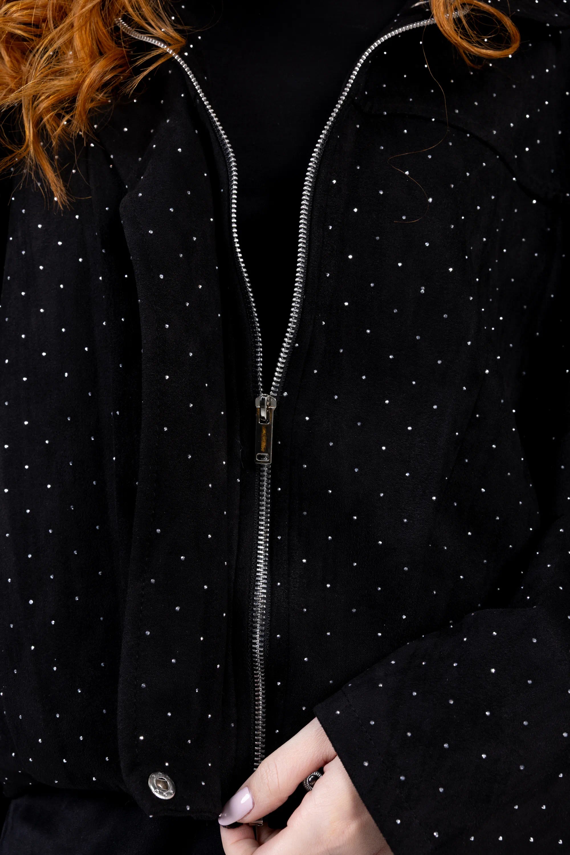 Close-up of a black jacket with white polka dots and a hand holding the zipper.
