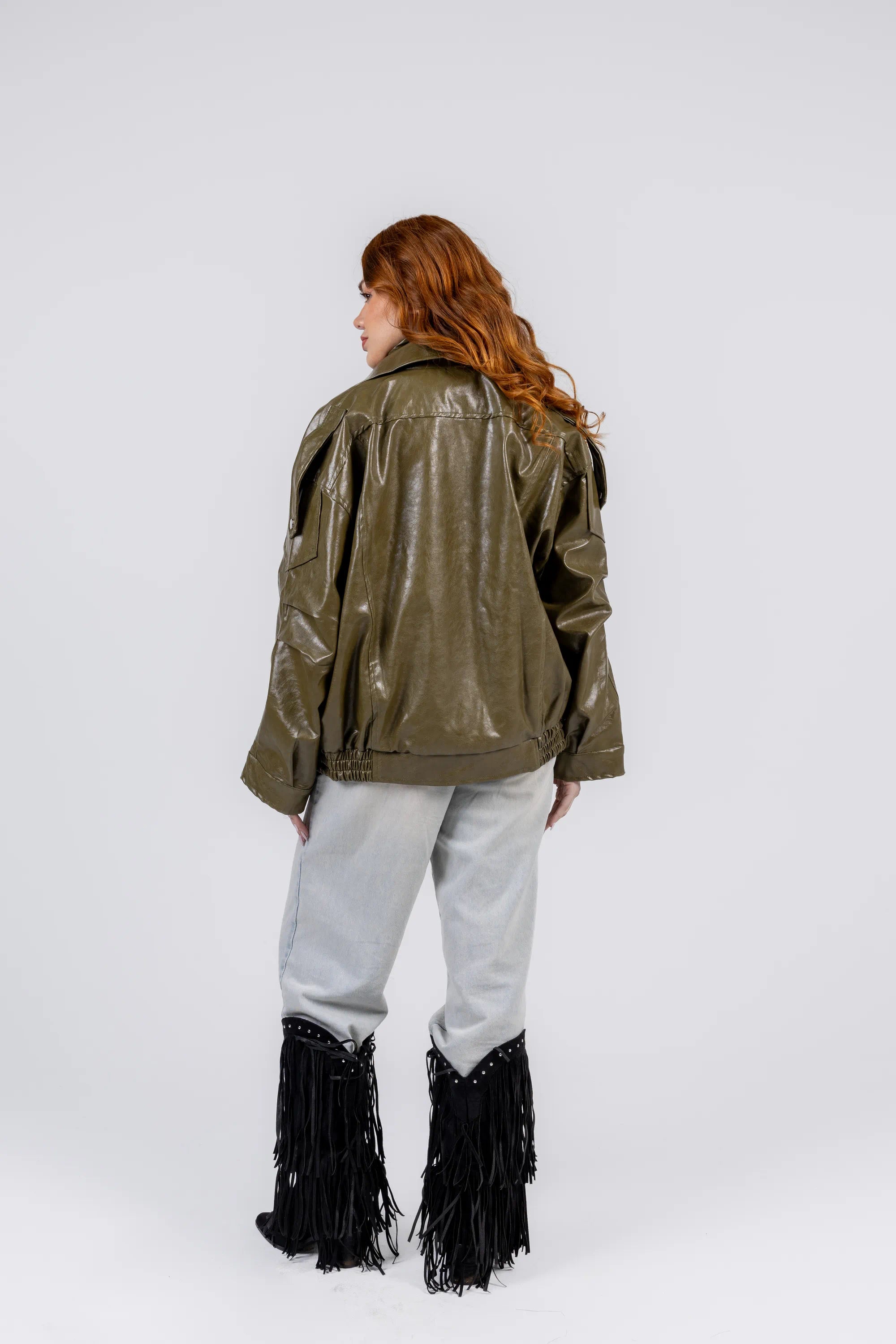 Person wearing a green shiny jacket and light gray pants with black fringed boots on a white background