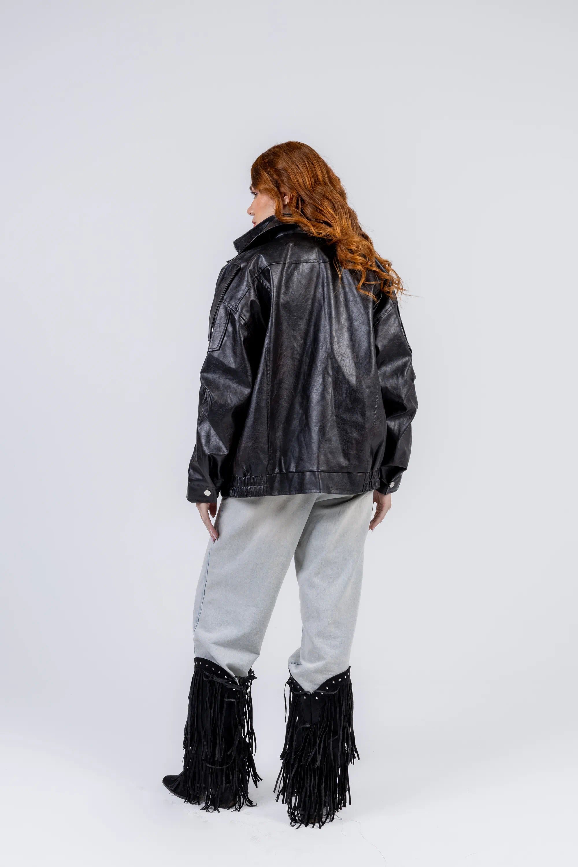 Person wearing a black leather jacket with fringe details on a white background