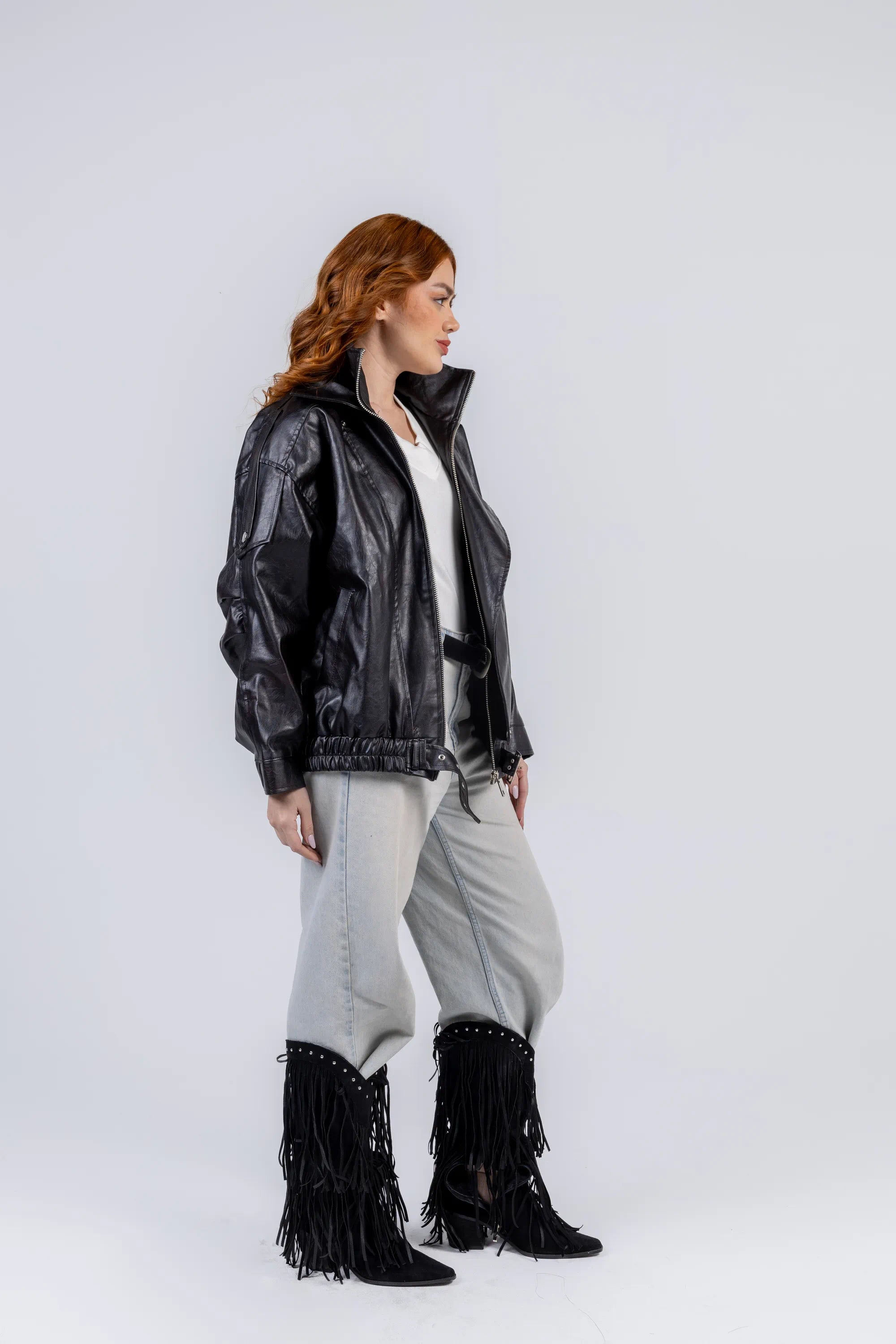 Person wearing a black jacket, white top, gray pants, and black fringed boots on a white background