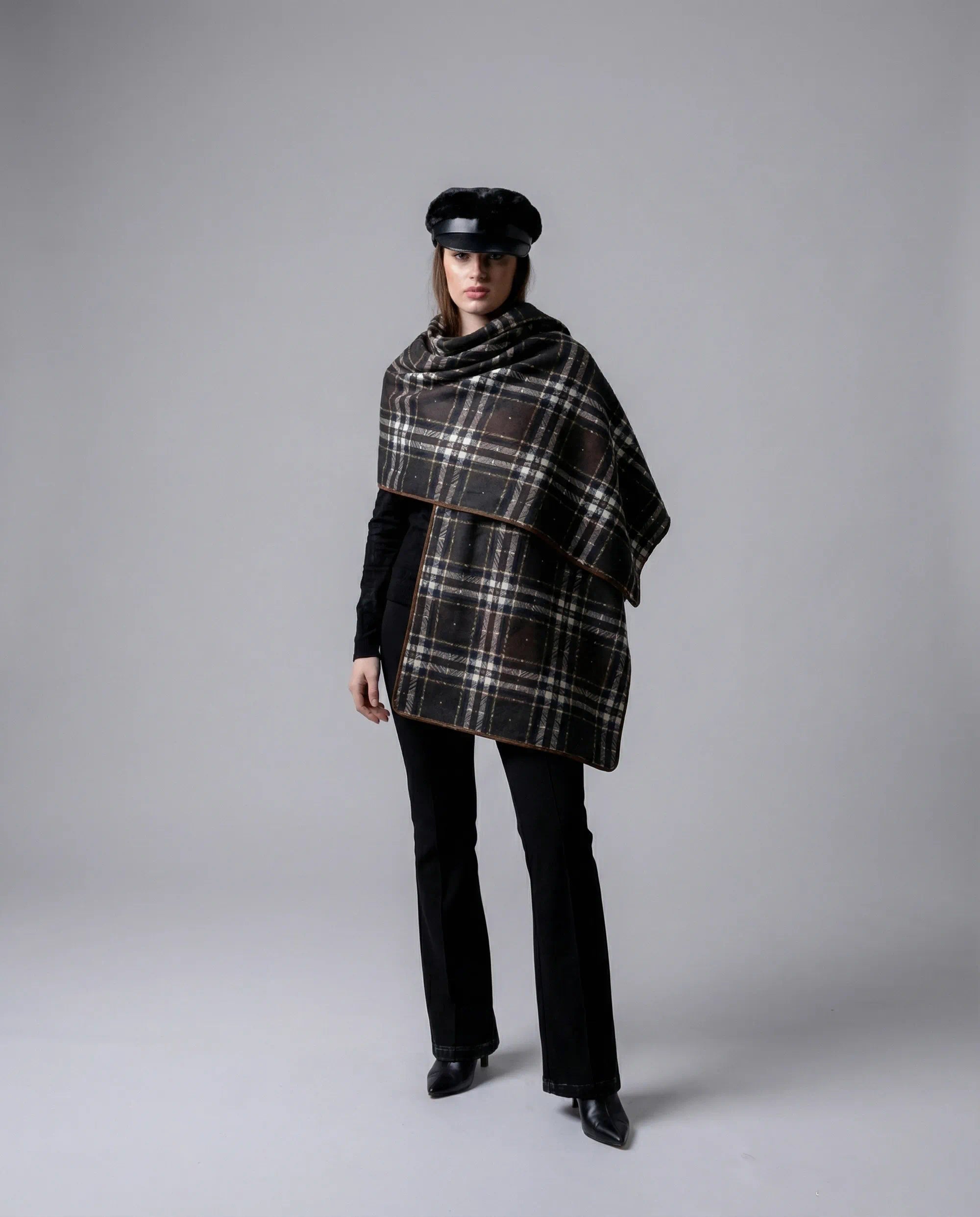 Person wearing a plaid poncho and black outfit on a gray background