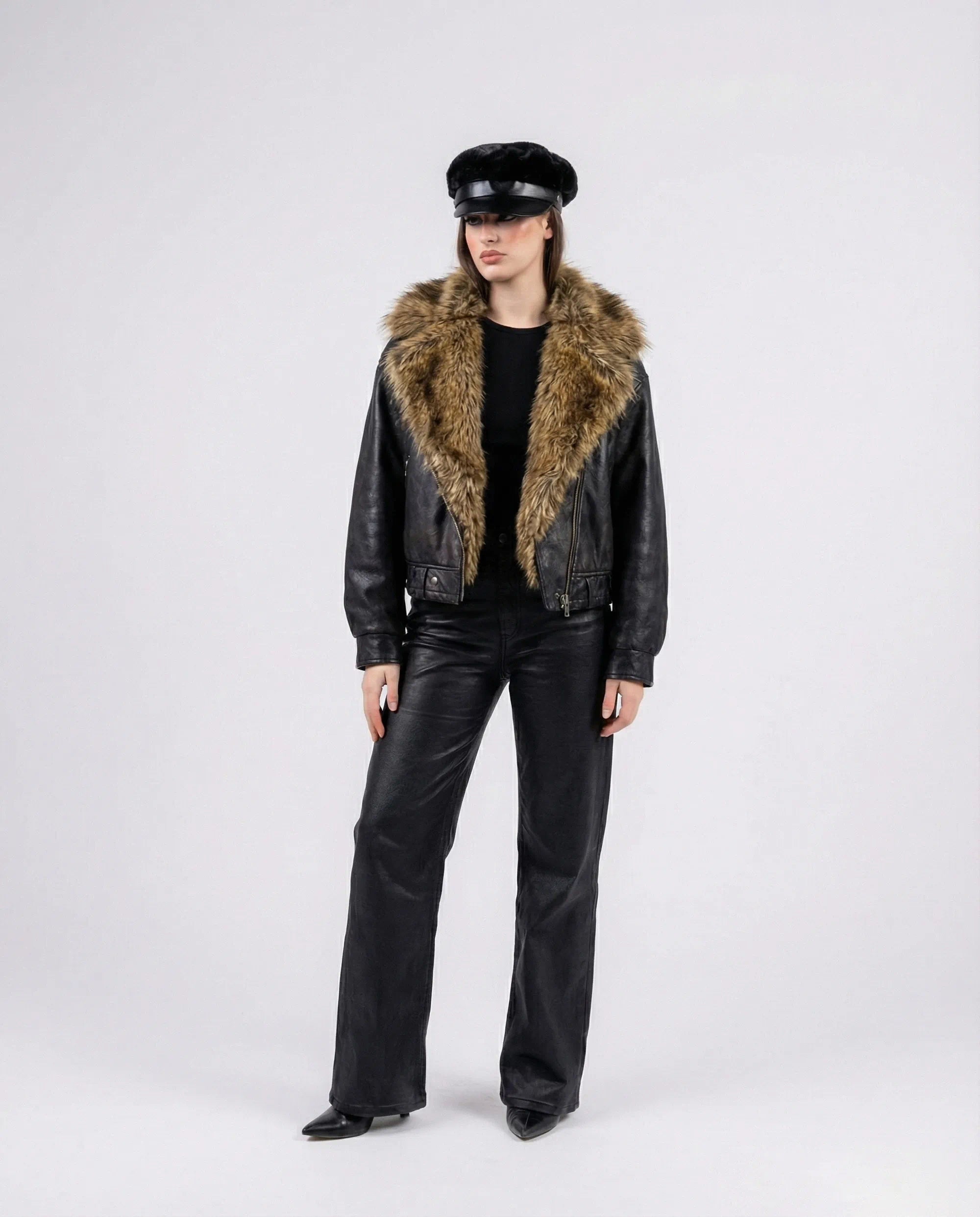 Person wearing a black leather jacket with fur collar and matching pants on a white background